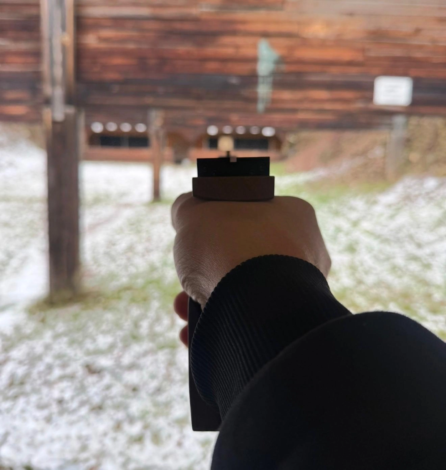 Schützenverein Bissingen/Enz e.V. – Blick über die Schulter auf eine Hand, die auf einem verschneiten Schießstand im Freien mit einer Pistole zielt.