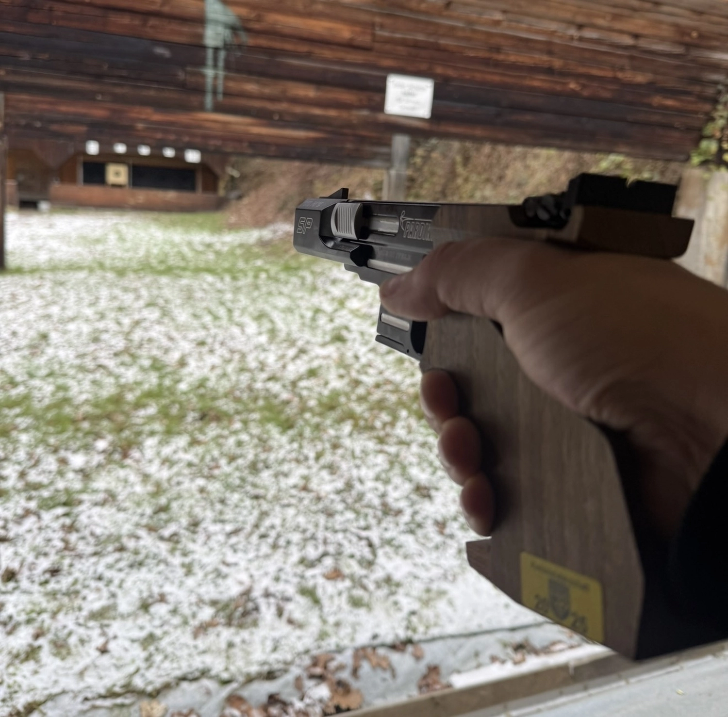 Schützenverein Bissingen/Enz e.V. – Eine Hand, die eine Pistole hält und auf eine Zielscheibe auf einem verschneiten Schießstand im Freien zielt.