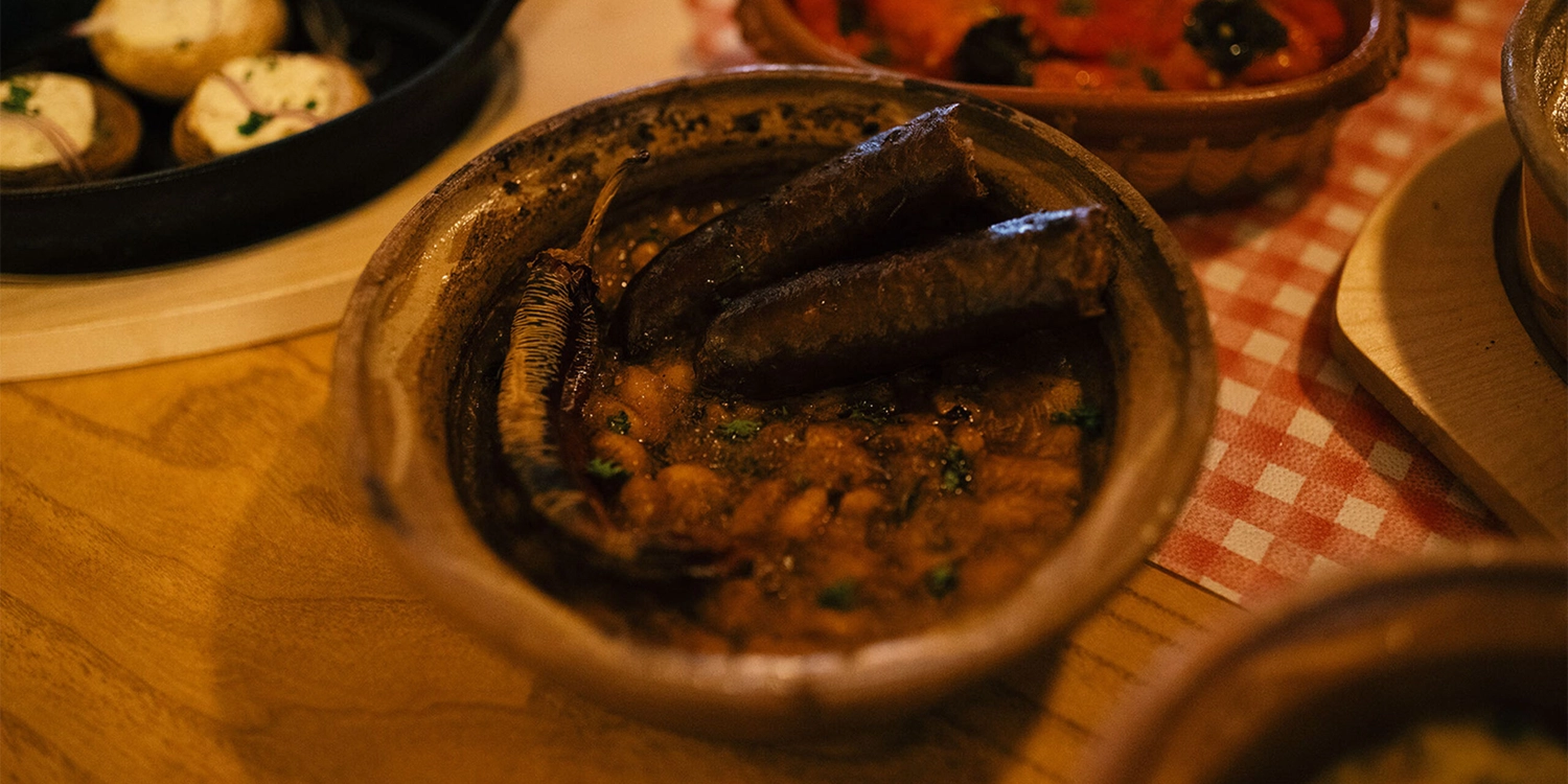 Schützenverein Bissingen/Enz e.V. – Eine rustikale Tonschale mit gebackenen Bohnen, zwei Würstchen und einer gerösteten Paprika obenauf, serviert auf einem Holztisch.