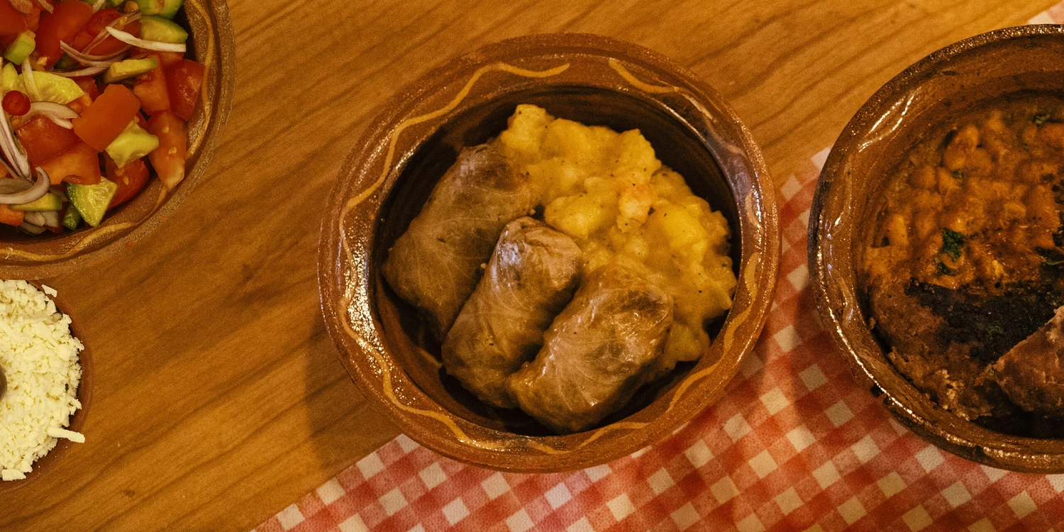 Schützenverein Bissingen/Enz e.V. – Eine Tonschüssel mit drei gefüllten Kohlrouladen, serviert mit Kartoffeln auf einem Holztisch mit einer rot karierten Serviette.